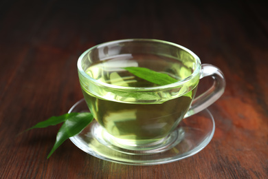 Cup of aromatic green tea and leaves on wooden table