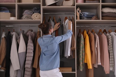 Photo of Young woman choosing clothes in wardrobe closet, back view