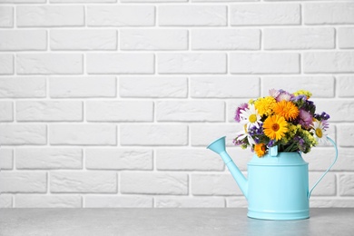 Photo of Watering can with beautiful wild flowers on table near brick wall