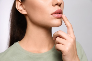 Woman with herpes touching lips on light grey background, closeup