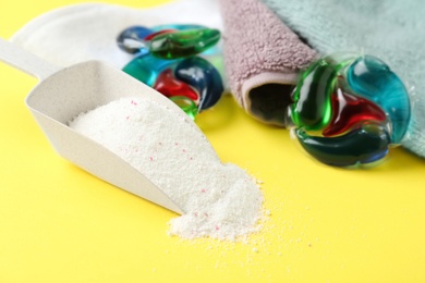Laundry capsules, scoop of washing powder and towels on yellow background, closeup