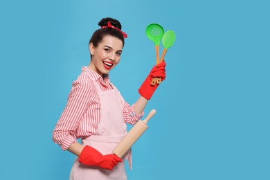 Photo of Young housewife with cooking utensils on light blue background