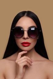 Attractive woman in fashionable sunglasses touching her face against beige background