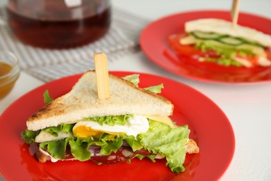 Photo of Delicious sandwich with vegetables, egg and salami on white table, closeup