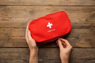 Woman opening first aid kit bag at wooden table, top view