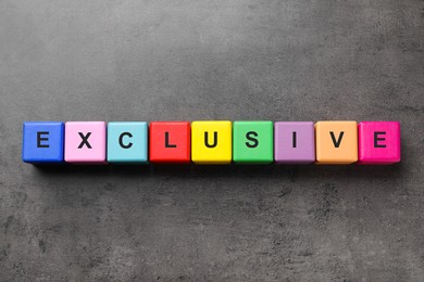 Photo of Colorful cubes with word Exclusive on dark grey background, flat lay