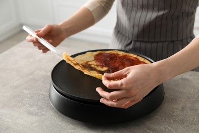 Photo of Woman cooking delicious crepe with jam on electric pancake maker in kitchen, closeup