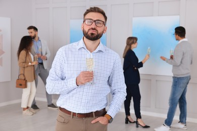 Young man with glass of champagne at exhibition in art gallery