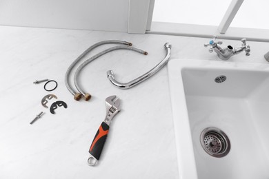 Photo of Parts of water tap and wrench on white marble countertop in kitchen