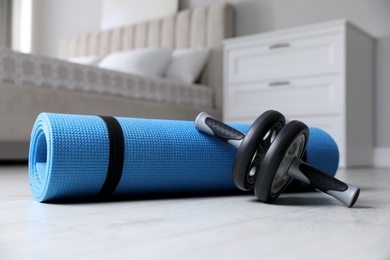 Abs roller and yoga mat on floor indoors. Fitness at home