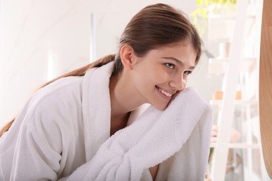 Beautiful teenage girl wiping face with towel in bathroom
