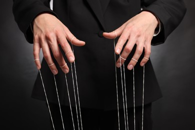 Woman in suit pulling strings of puppet on dark background, closeup