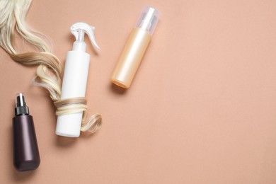 Photo of Spray bottles with thermal protection and lock of blonde hair on beige background, flat lay. Space for text