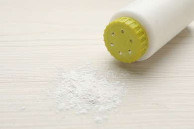 Photo of Bottle and scattered dusting powder on white wooden background. Baby cosmetic product