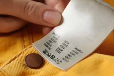 Woman reading clothing label with care symbols and material content on yellow jeans, closeup