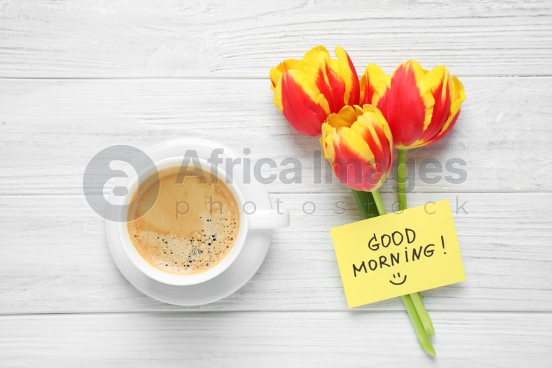 Delicious coffee, flowers and card with GOOD MORNING wish on white wooden table, flat lay