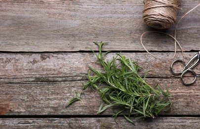 Fresh green rosemary, twine and scissors on wooden table, flat lay. Space for text