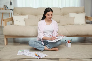 Young woman coloring antistress page near sofa in living room