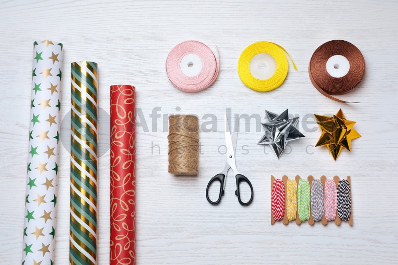 Photo of Flat lay composition with colorful wrapping paper rolls and accessories on white wooden table
