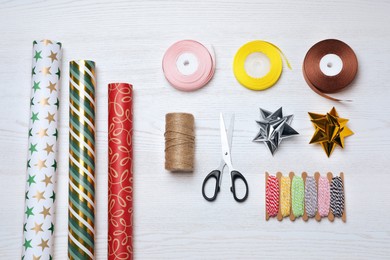 Flat lay composition with colorful wrapping paper rolls and accessories on white wooden table