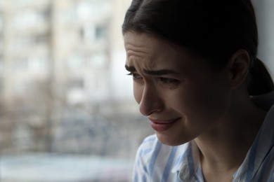Sad young woman crying near window indoors, closeup with space for text. Loneliness concept