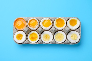 Photo of Boiled chicken eggs of different readiness stages in carton on light blue background, top view