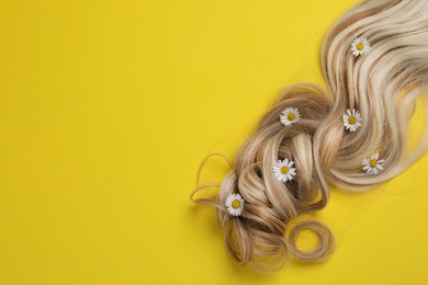 Lock of healthy blond hair with flowers on yellow background, top view. Space for text