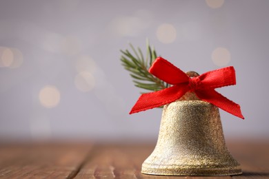 Photo of Bell with red bow on wooden table against blurred background, closeup and space for text. Christmas decor