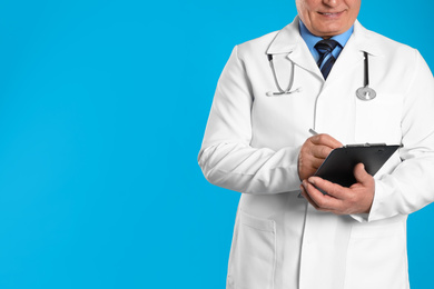 Senior doctor with clipboard on light blue background, closeup. Space for text