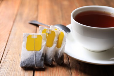 Tea bags near cup of hot drink on wooden table, closeup