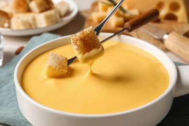 Dipping pieces of bread into tasty cheese fondue at table, closeup