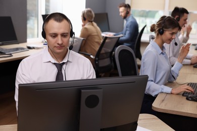 Call center operators working in modern office, focus on young man with headset