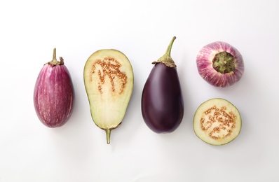 Cut and whole raw ripe eggplants on white background, flat lay