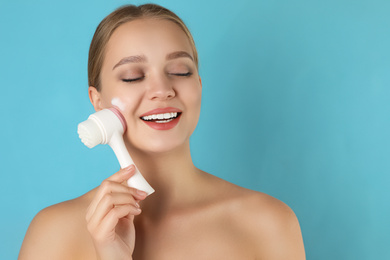 Young woman washing face with brush and cleansing foam on light blue background. Cosmetic products