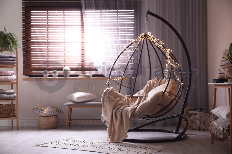 Photo of Cozy hanging chair with fairy lights in modern living room. Interior design
