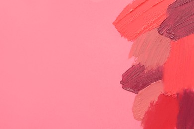Smears of different beautiful lipsticks on pink background, top view. Space for text