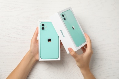 Photo of MYKOLAIV, UKRAINE - JULY 10, 2020: Woman opening box with new modern Iphone 11 Green at white wooden table, top view