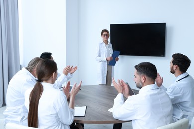 Photo of Team of doctors listening to speaker report near tv screen in meeting room. Medical conference