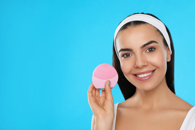Young woman holding facial cleansing brush on light blue background, space for text. Washing accessory