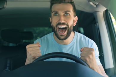 Stressed angry man in driver's seat of modern car, view through windshield