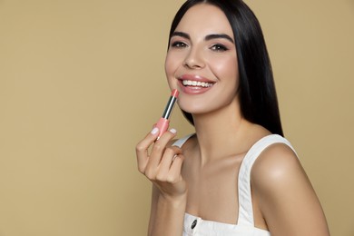 Young woman with beautiful makeup holding nude lipstick on beige background, space for text