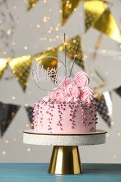 Beautifully decorated birthday cake and party decor on turquoise wooden table against blurred festive lights