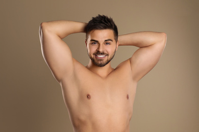 Young man showing hairless armpits after epilation procedure on brown background