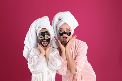 Emotional mother and daughter with black facial masks on pink background