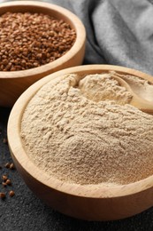Buckwheat flour and grains in bowls on black table, closeup