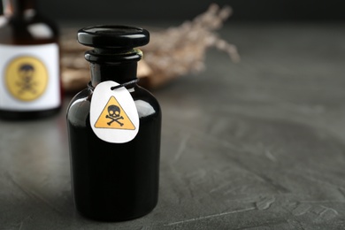 Glass bottle of poison with warning sign on grey stone table. Space for text