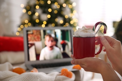 MYKOLAIV, UKRAINE - DECEMBER 25, 2020: Woman with sweet drink watching Home Alone movie on laptop indoors, closeup. Cozy winter holidays atmosphere