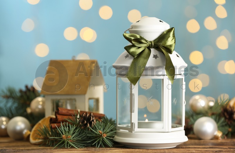 Photo of Christmas lantern with burning candle and festive decor on wooden table against blurred lights