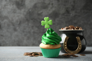 Decorated cupcake and pot with gold coins on grey wooden table, space for text. St. Patrick's Day celebration