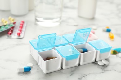 Plastic box with different pills on white marble table